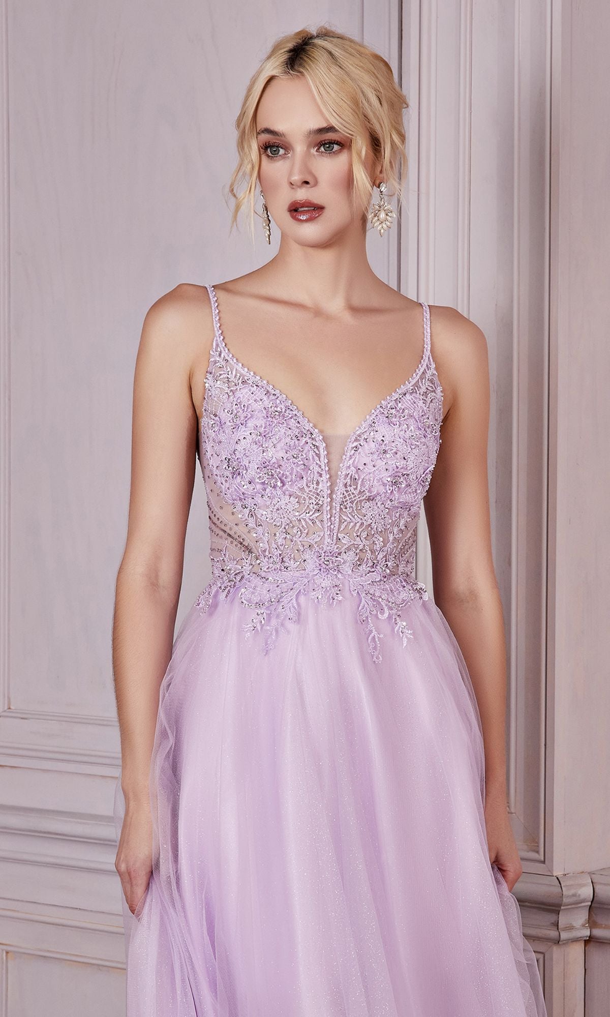 A woman stands against a pale wooden wall wearing the Embellished-Bodice Long Tulle Prom Dress CD0195, featuring a sleeveless light purple deep v-neck, intricate beading, and a long tulle A-line skirt.